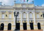 Fachada neoclásica amarilla del Teatro Municipal Enrique Buenaventura en Cali con banderas de Colombia, Cali y Valle del Cauca, y escaleras de acceso.