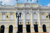 Fachada neoclásica amarilla del Teatro Municipal Enrique Buenaventura en Cali con banderas de Colombia, Cali y Valle del Cauca, y escaleras de acceso.