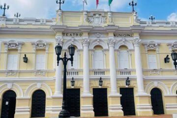Fachada neoclásica amarilla del Teatro Municipal Enrique Buenaventura en Cali con banderas de Colombia, Cali y Valle del Cauca, y escaleras de acceso.