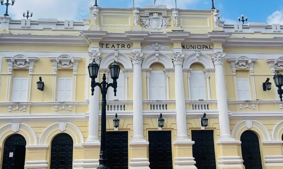 Fachada neoclásica amarilla del Teatro Municipal Enrique Buenaventura en Cali con banderas de Colombia, Cali y Valle del Cauca, y escaleras de acceso.